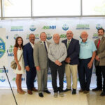 Pictured standing in front on ASU-Mountain Home backdrop are (from left) Heather Maxey, ASU System Board of Trustees; Dr. Todd Shields, ASU System President; Dr. Bentely Wallace, ASUMH Chancellor; Dr. Roger Simons, donor; Wes Henderson, Yellville-Summit School District Superintendent; Richard Blevins, Norfork School District Superintendent; Kelvin Hudson, Flippin School District Superintendent; Jayme Jones, Cotter Public School District Superintendent