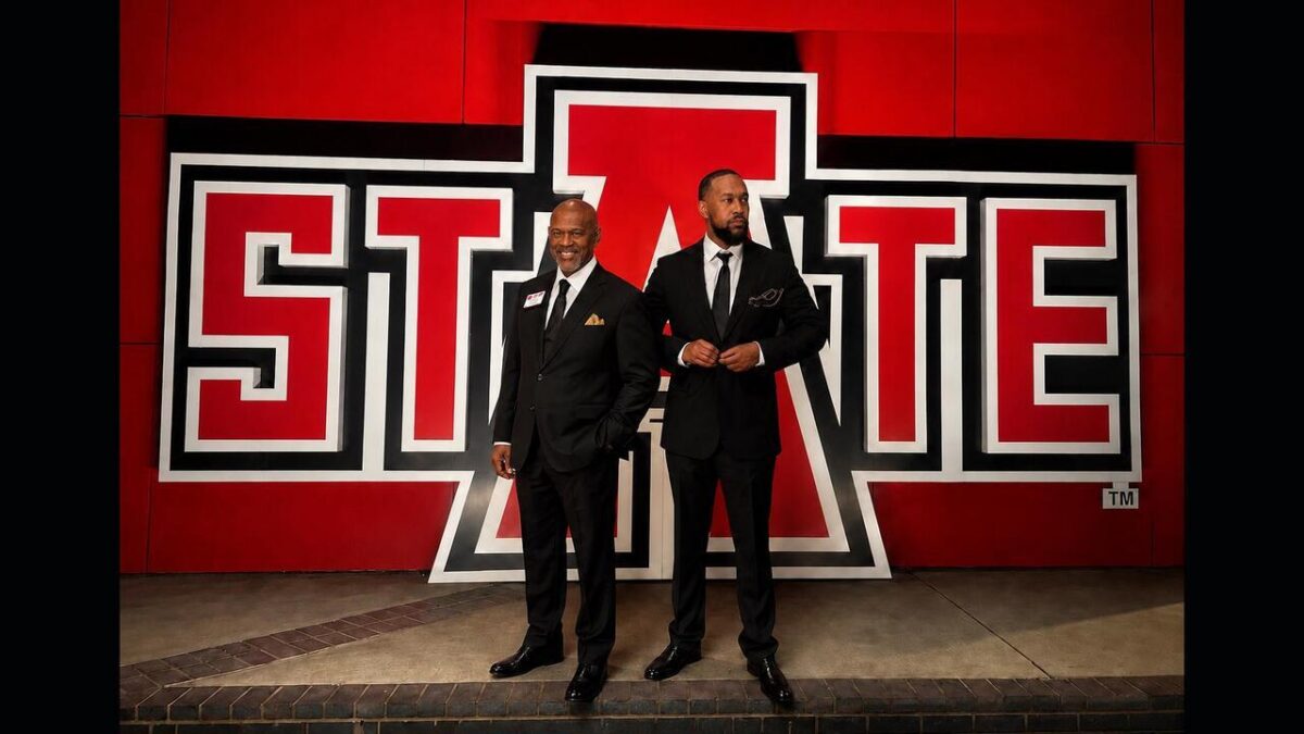 Picture of A-State alumni Ronald and Mitchell Dedman standing in front of A-State logo sign
