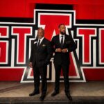Picture of A-State alumni Ronald and Mitchell Dedman standing in front of A-State logo sign